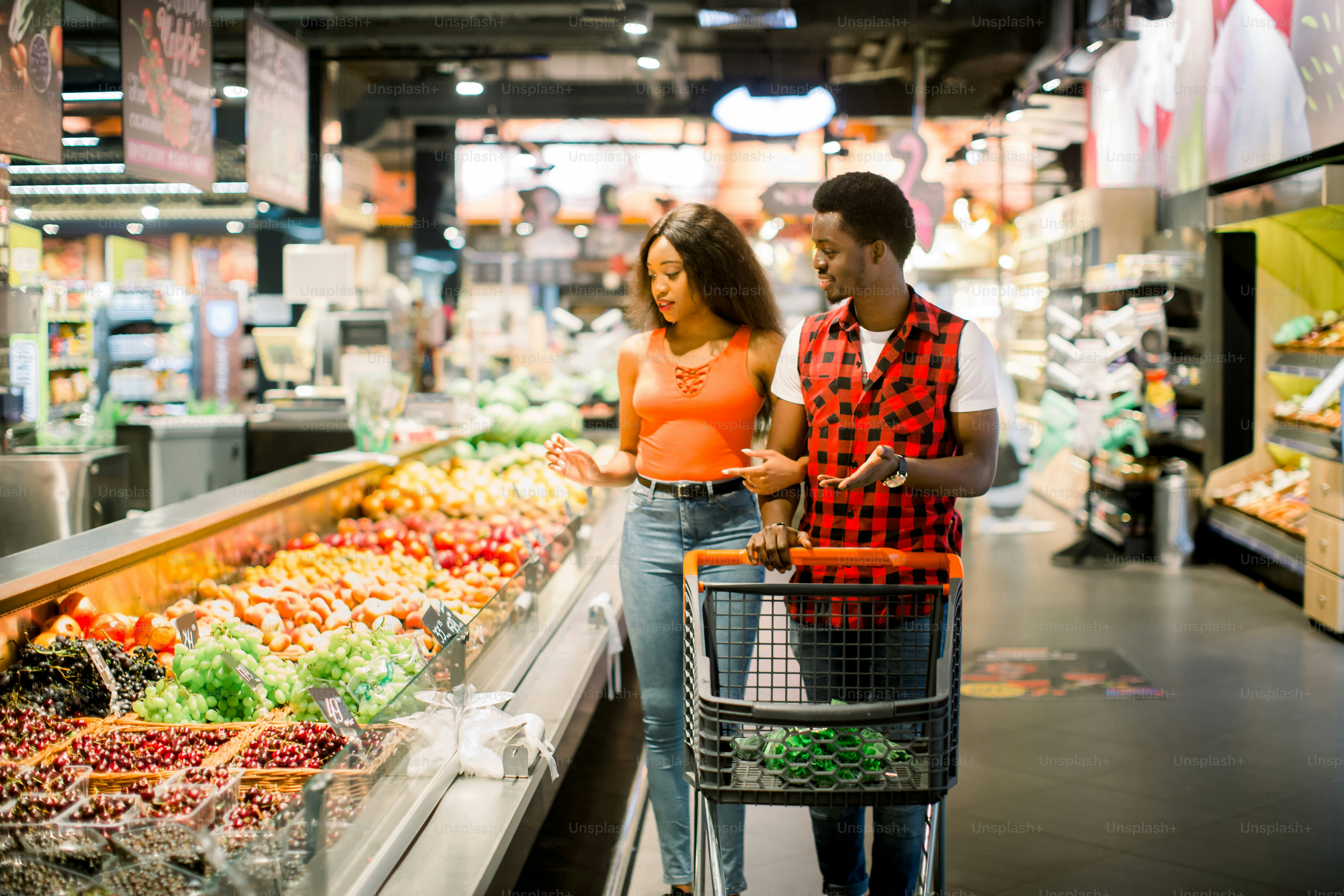 smiling african american couple with shopping trolley choosing food in supermarket