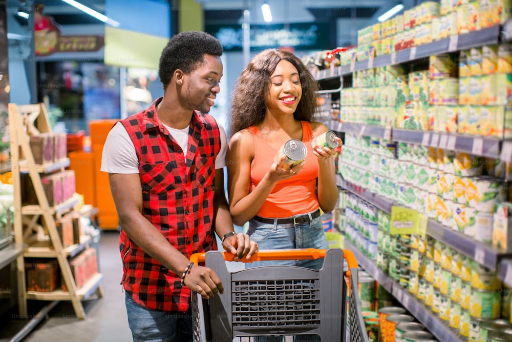 smiling african american couple with shopping trolley choosing food in supermarket