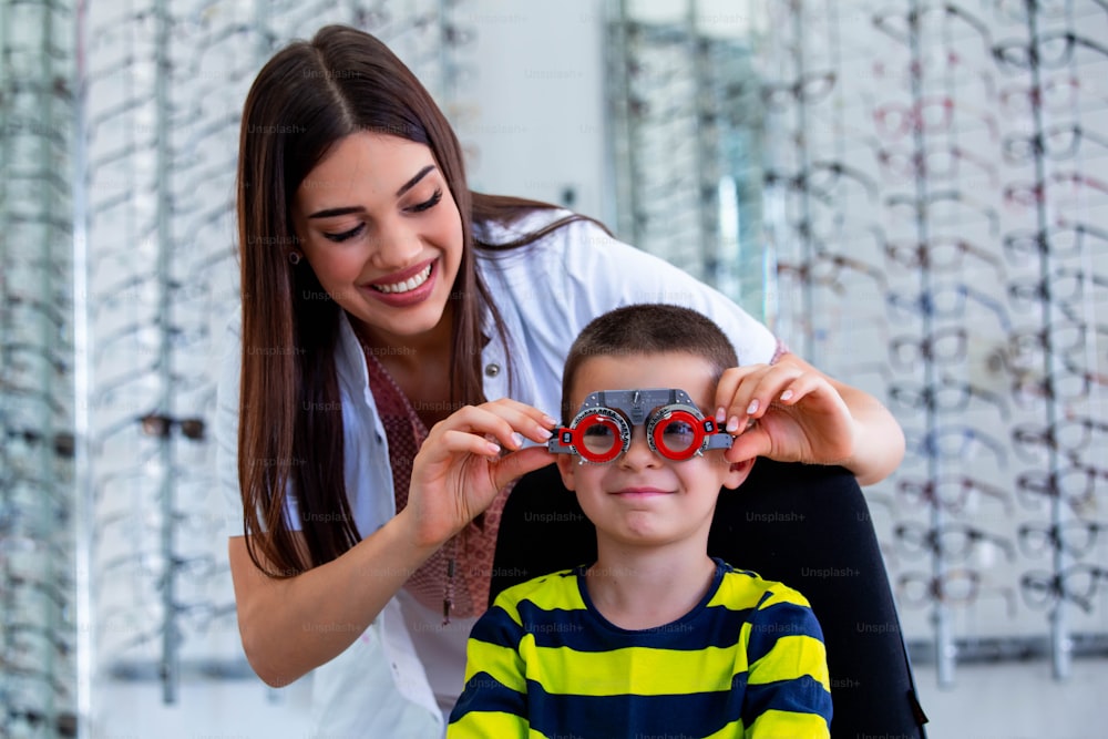 魅力的な眼科医は、検眼医の試験フレームでyoug少年を診察します。眼科クリニックで視力を確認する小児患者。