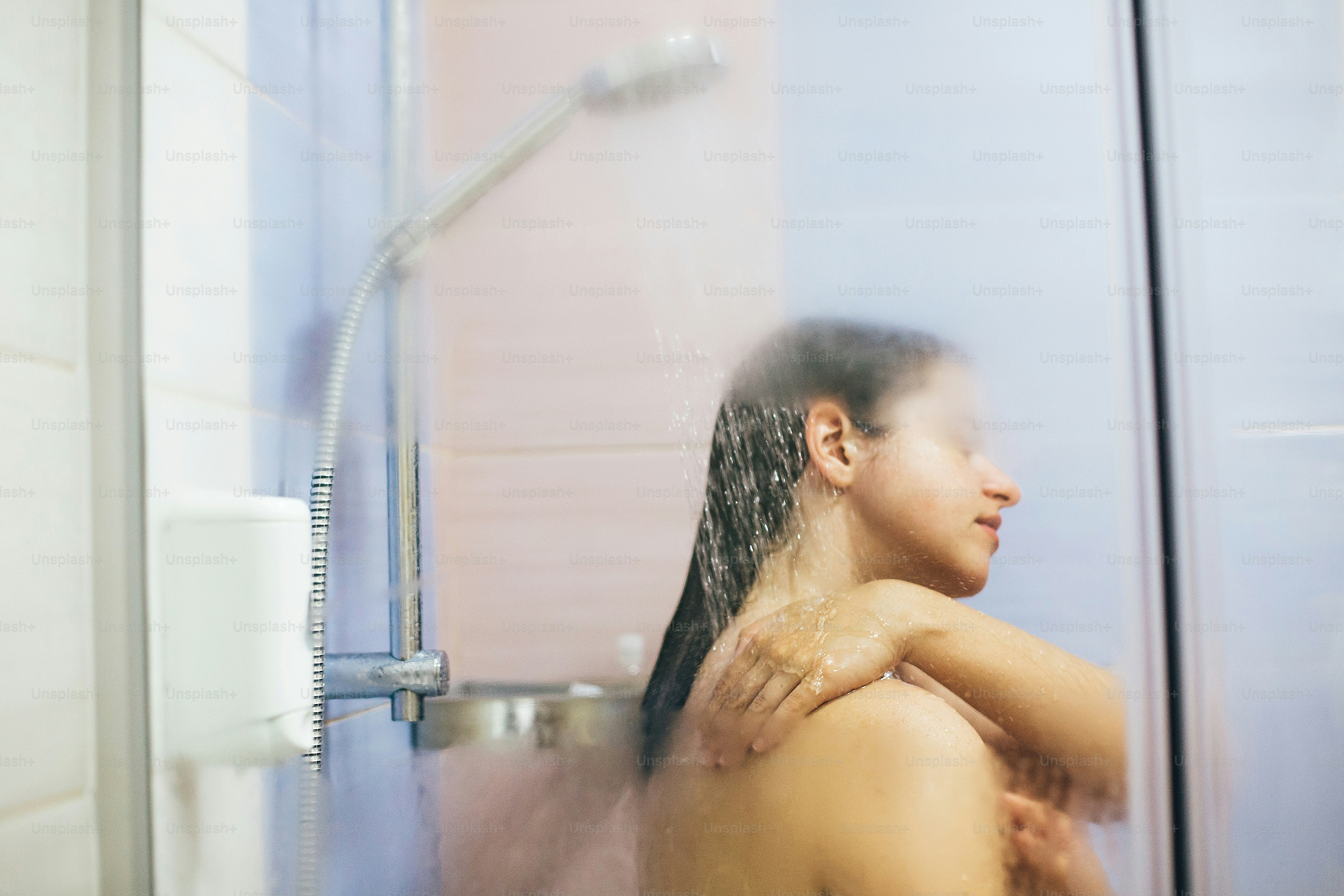 Young happy woman taking hot shower at home or hotel bathroom. Sensual portrait of beautiful brunette girl enjoying time in shower. Body and skin hygiene, lifestyle concept. Space text