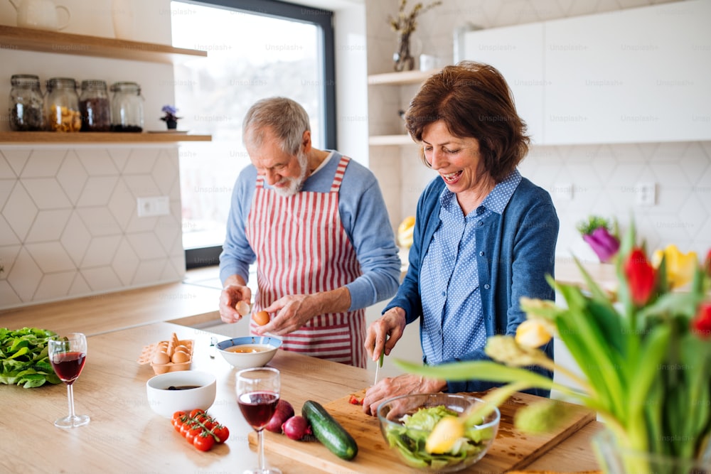 Un retrato de una feliz pareja de ancianos enamorada en casa, cocinando.