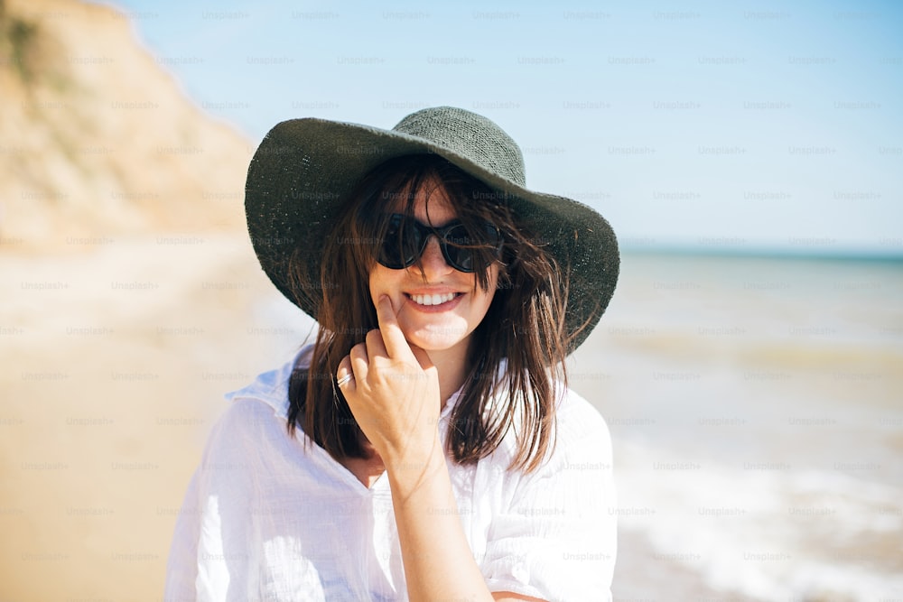 Summer vacation. Happy young boho woman walking in sea waves in sunny warm day at tropical island and blue sky. Space for text. Stylish hipster girl in hat  relaxing on beach and smiling.