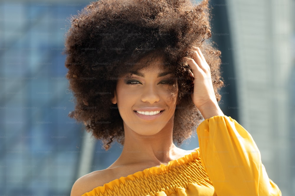 Portrait of young african american woman with curly hair posing in the city street.