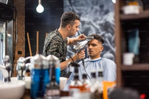 Close-up, master Barber does the hairstyle and styling with dryer, dries hair to guy. Concept Barbershop. Soft focus.