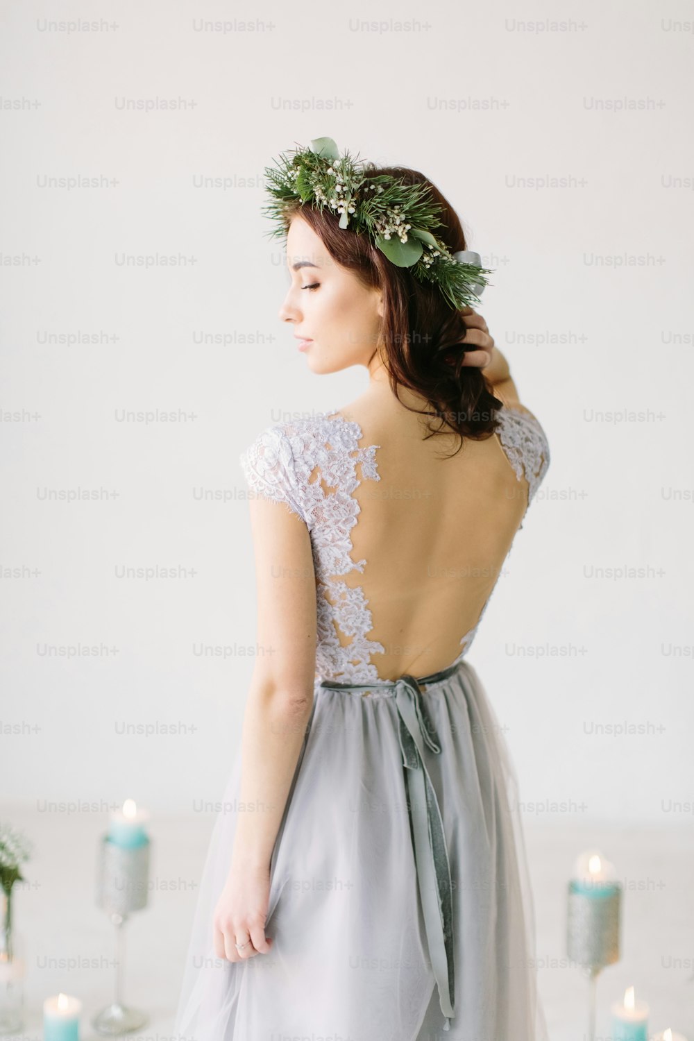 Beautiful young girl in a gray evening dress and a wreath of pine and eucalyptus on her head poses on the background of wedding scenery. Bridesmade poses in the studio before wedding ceremony.