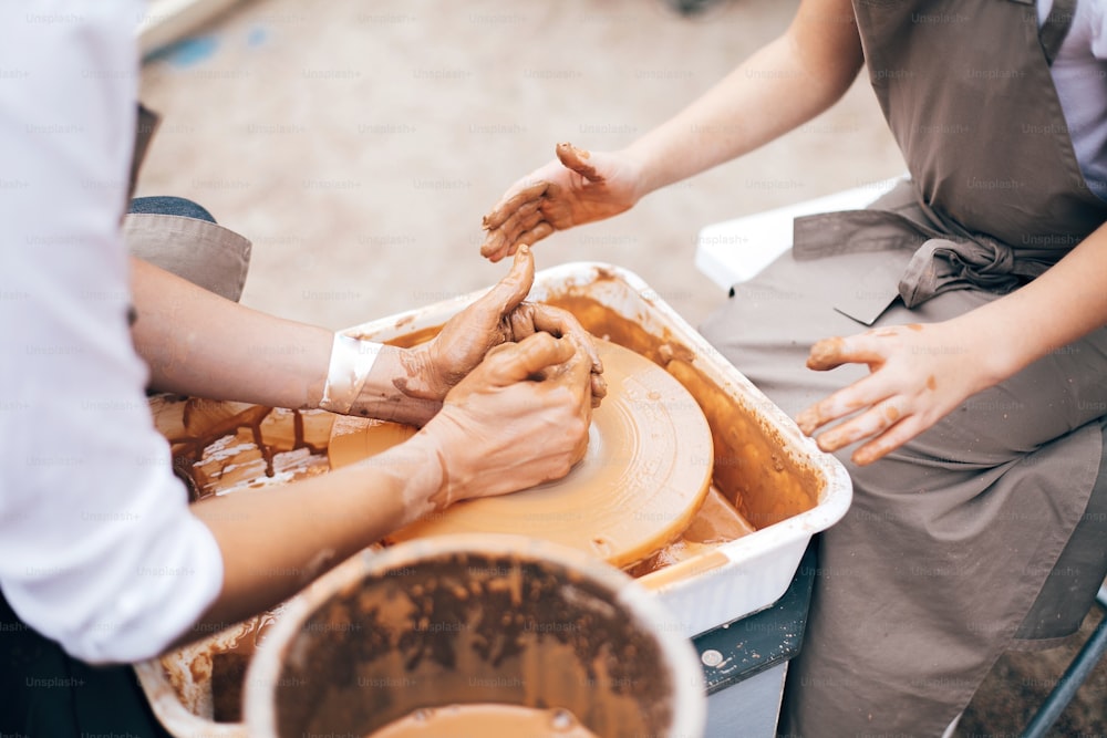 Pottery workshop. Hands of adult and child making pottery, working with wet clay closeup. Process of making bowl from clay on wheel with dirty hands. Handmade festival in summer park