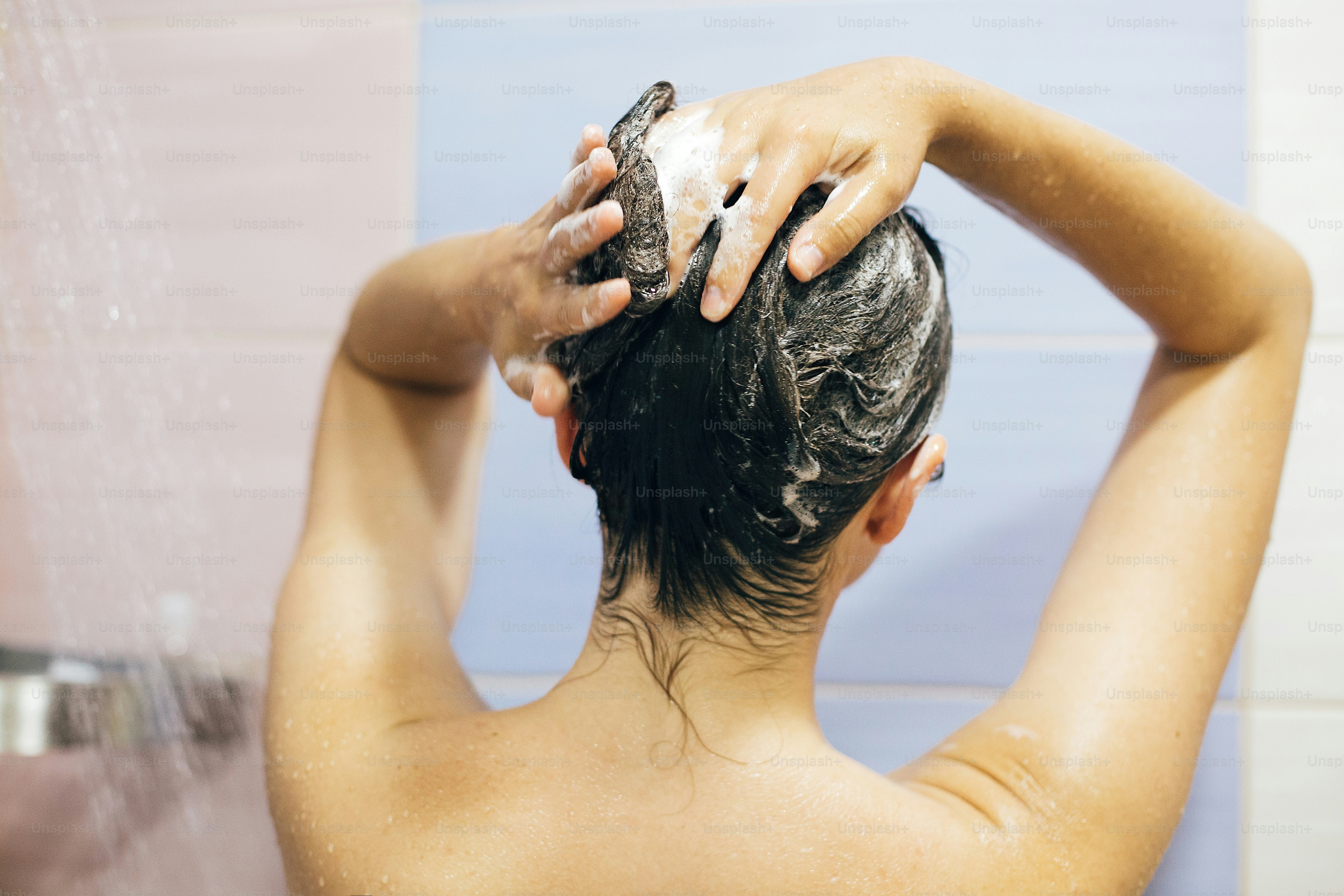 Young happy woman washing her hair with shampoo, hands with foam closeup. Back of beautiful brunette girl taking shower and enjoying relax time. Body and hair hygiene, lifestyle concept