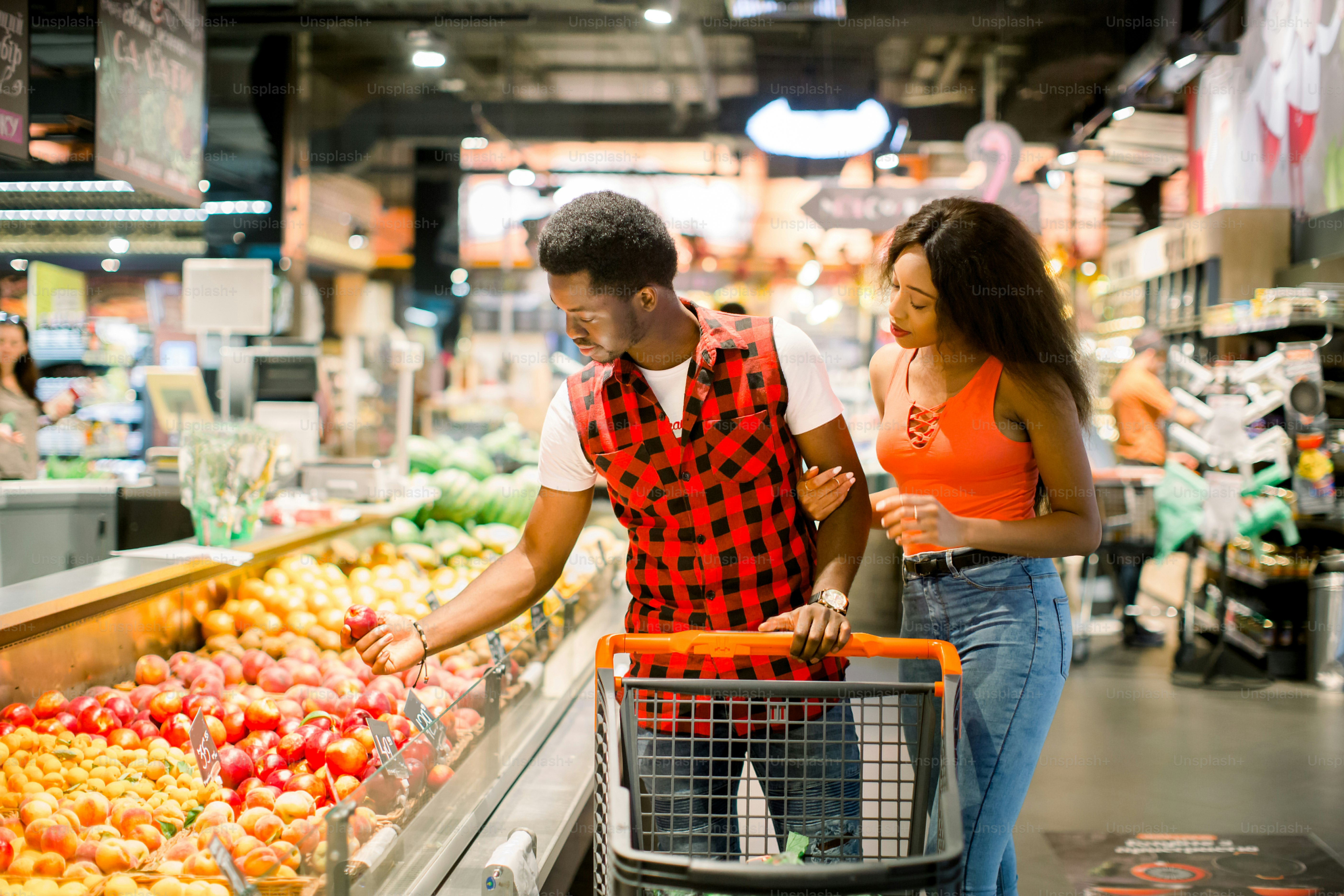 smiling african american couple with shopping trolley choosing food in supermarket