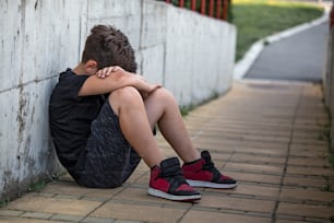 Little boy sad sitting alone at school hides his face. Isolation and bullying concept. Kid sad and unhappy, child was crying, upset, feel sick