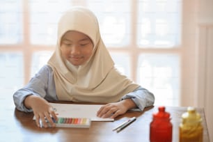 Asiatisches muslimisches Mädchen, das im Kunstunterricht auf Papier zeichnet.