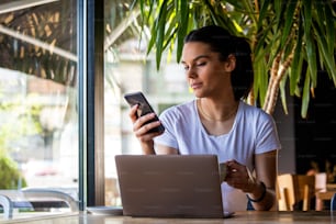 Smiling woman drinking coffee and using her mobile phone. Satisfied female enjoying cup of coffee. Close up portrait of beautiful girl drinking coffee from a white mug in the coffee shop