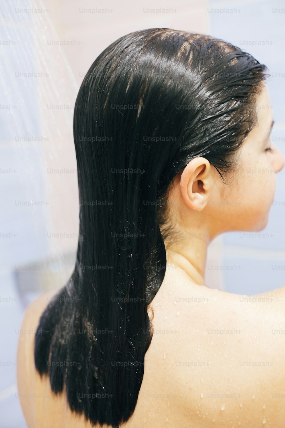 Young happy woman taking shower at home or hotel bathroom. Wet hair. Beautiful  brunette girl washing her hair and enjoying relax time. Body and skin hygiene, lifestyle concept