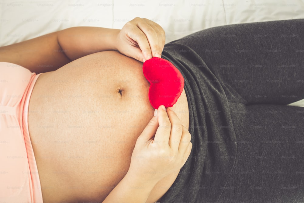 Pregnant woman feeling happy at home while taking care of her child. The young expecting mother holding baby in pregnant belly. Maternity prenatal care and woman pregnancy concept.