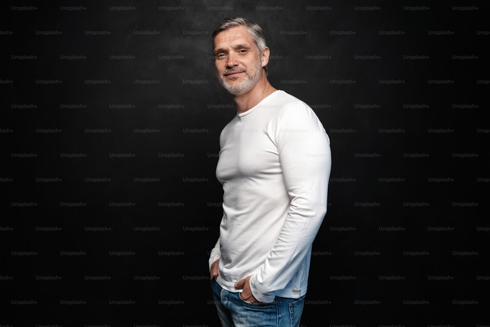 Hombre guapo de mediana edad con camiseta blanca posando frente a un fondo negro con espacio de copia