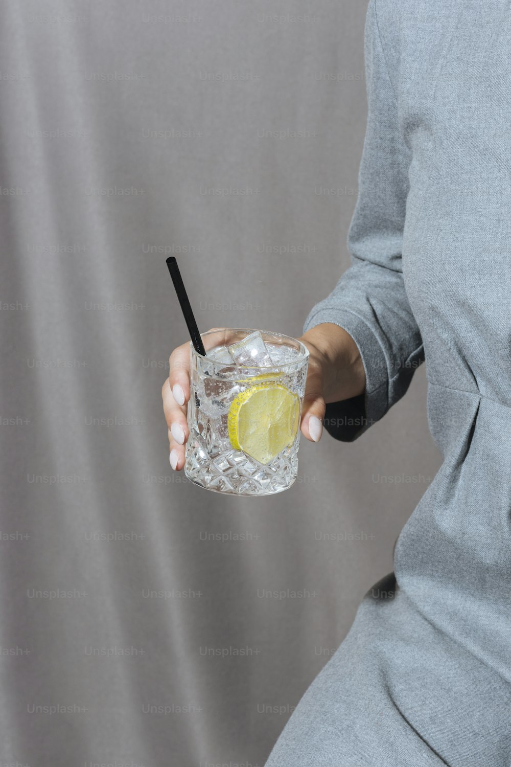 Mujer sosteniendo gin tonic, fondo gris y malhumorado