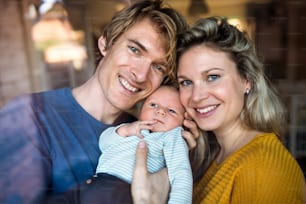 Beautiful young parents holding a newborn baby at home. Shot through glass.