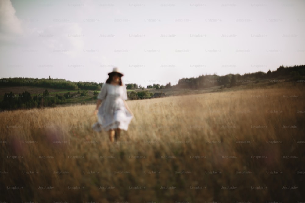Herbs and wildflowers in sunny meadow in mountains and blurred image of girl in linen dress walking. Boho woman relaxing in countryside, simple rustic life style. Atmospheric image