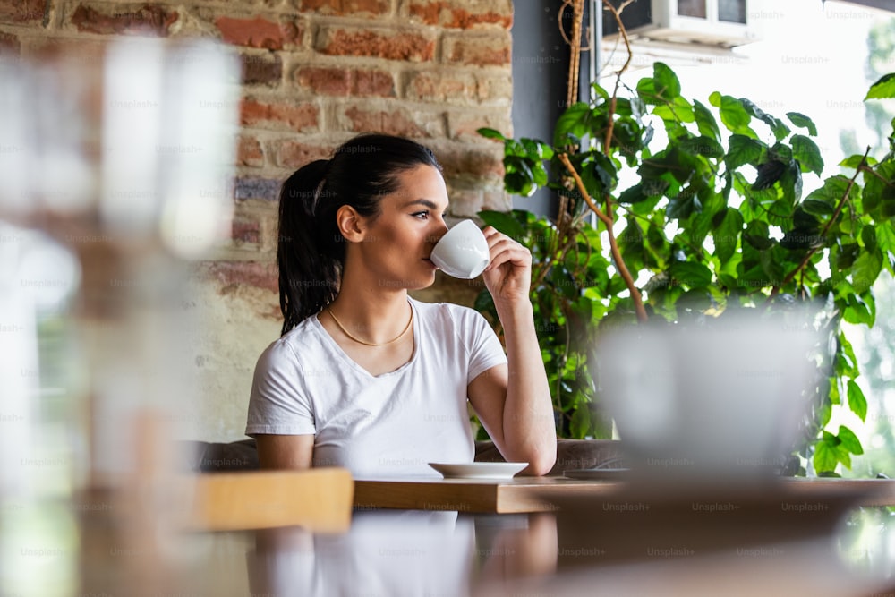 Schöne junge Frau mit Tasse Kaffee. Frau genießt frischen Kaffee am Morgen mit Sonnenaufgang im Café Schöne Frau, die morgens Kaffee trinkt und am Fenster sitzt
