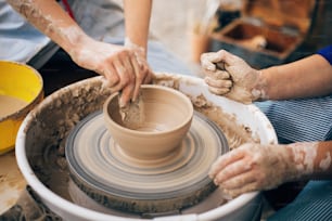 陶芸ワークショップ。大人と子供の手が陶器を作り、濡れた粘土の接写で作業します。汚れた手でろくろの上で粘土からボウルを作るプロセス。夏の公園で手作り祭り