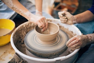 Mãos de adulto e criança fazendo cerâmica, trabalhando com closeup de barro molhado. Processo de fazer tigela de argila sobre roda com as mãos sujas. Festival artesanal no parque de verão. Oficina de cerâmica.