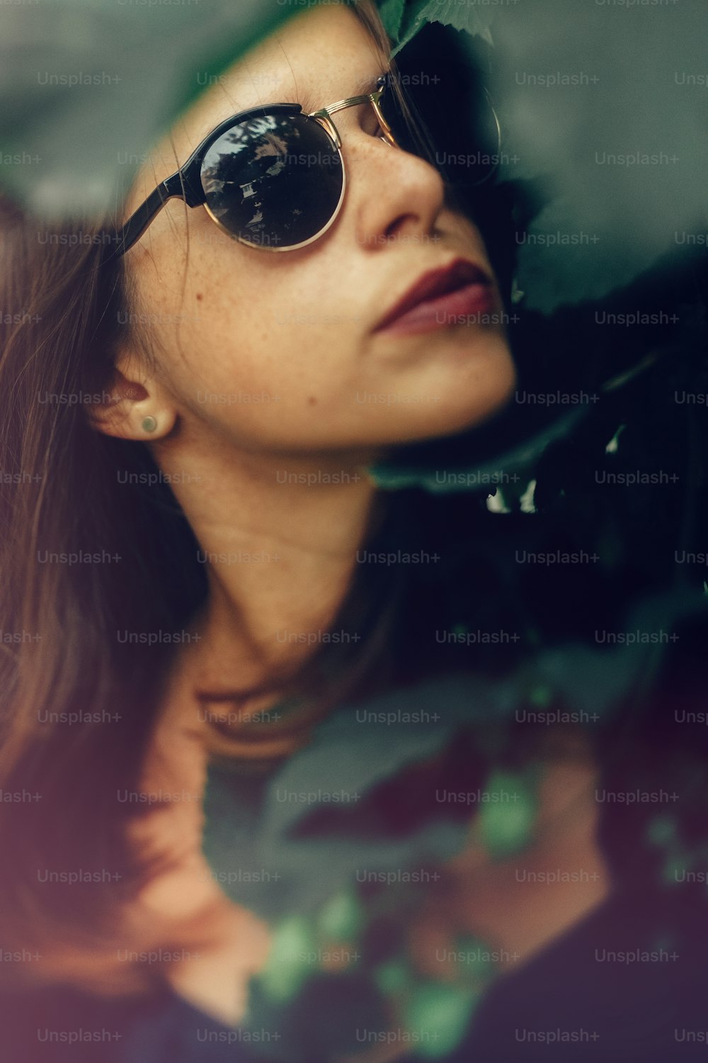 Stylish hipster girl posing at green hop bush, atmospheric moment. Portrait of fashionable cool woman in black sunglasses relaxing in park. Selective focus, creative image. Space for text