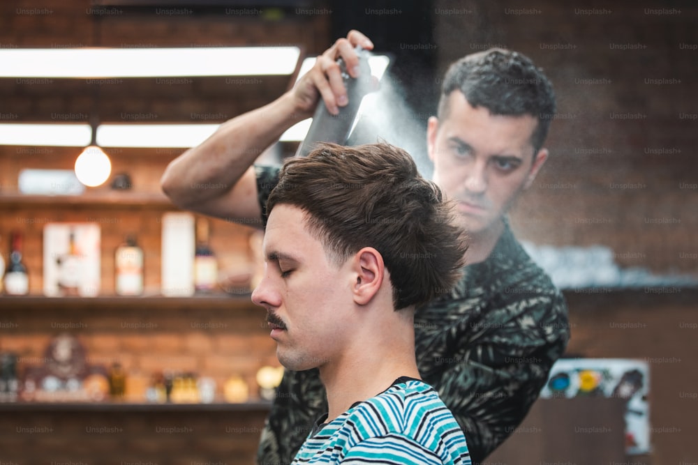 Professional Hairdresser using hair spray on client hair at barber shop, Cool barber splashes from the spray bottle at the hair of his client.