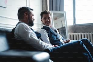 Relaxing. Full length of two young handsome men in suits holding glasses and looking at each other while resting indoors