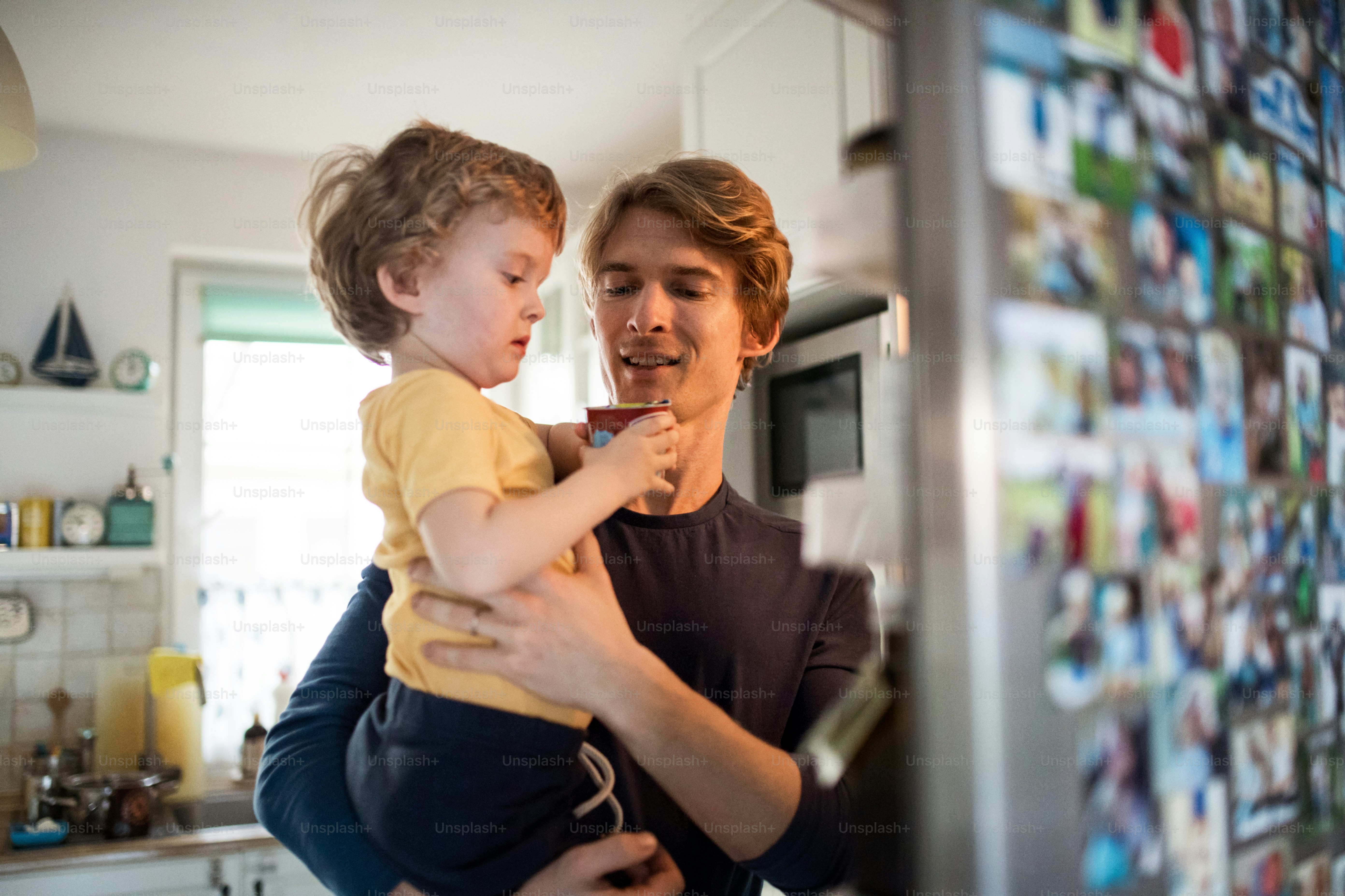 A happy father with a toddler son indoors in kitchen at home, opening fridge