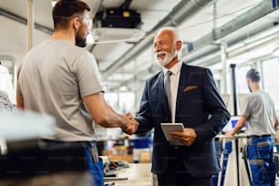 Happy senior businessman handshaking with manual worker in a factory.