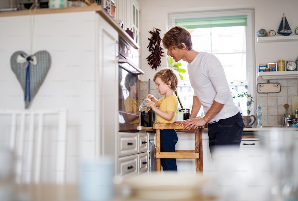 Um jovem pai com um filho pequeno passando o tempo em uma cozinha em casa.