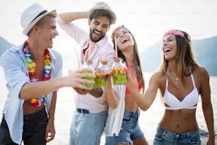 Group of friends having fun together at the beach and drinking cocktails