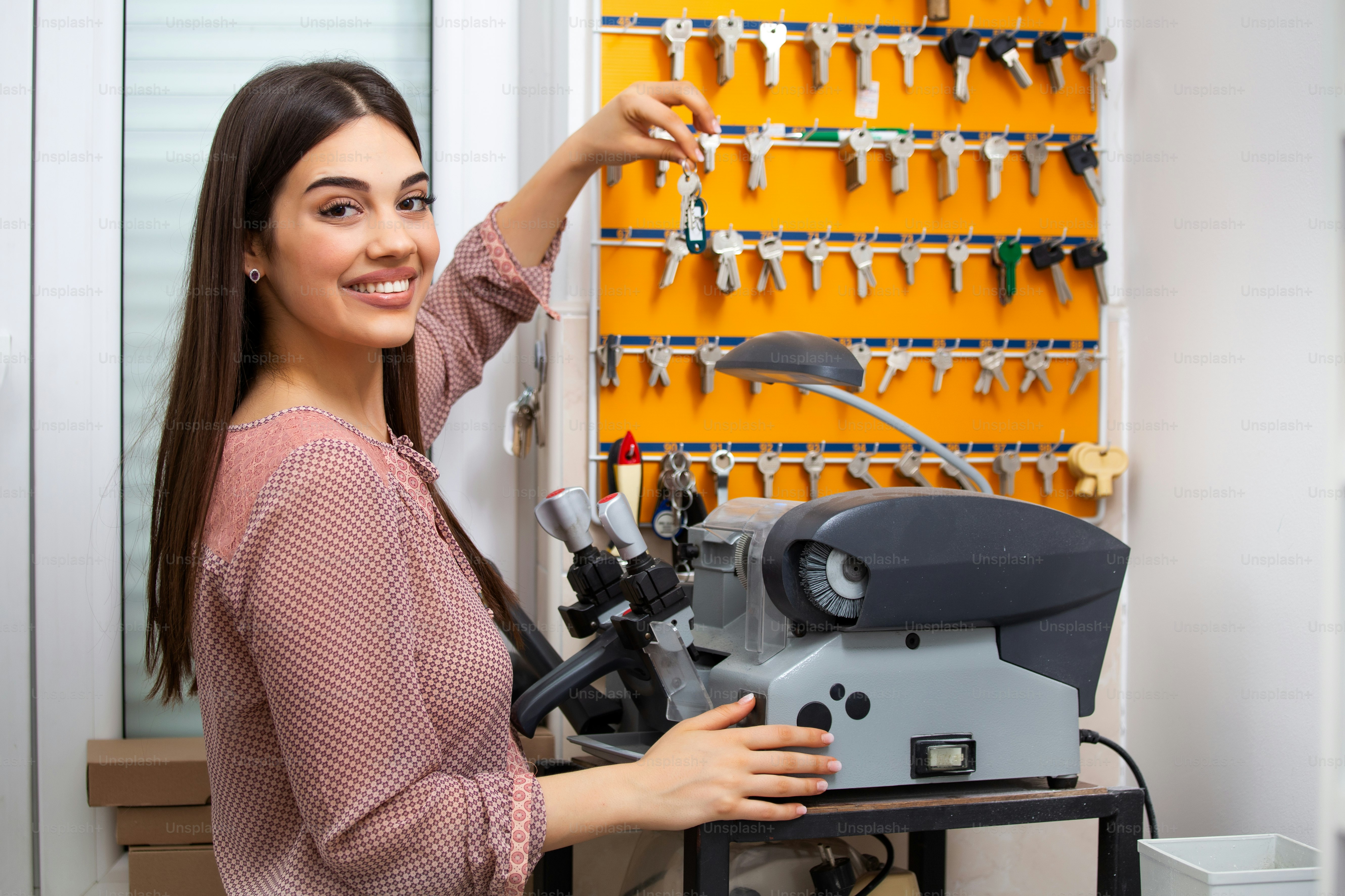 Professional skilled key cutter making door keys copies in locksmith. Young professional with different types of keys in locksmith