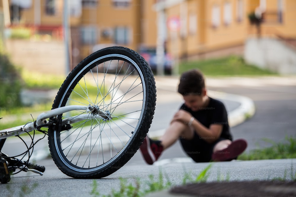 Kid hurts his leg after falling off his bicycle. Child is learning to ride a bike. Boy in the street ground with a knee injury screaming after falling off to his bicycle.