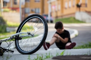 Kid hurts his leg after falling off his bicycle. Child is learning to ride a bike. Boy in the street ground with a knee injury screaming after falling off to his bicycle.