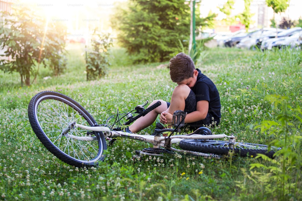 Kid si fa male a una gamba dopo essere caduto dalla bicicletta. Il bambino sta imparando ad andare in bicicletta. Ragazzo in strada con un infortunio al ginocchio che urla dopo essere caduto dalla sua bicicletta.