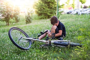 Kid se lastima la pierna después de caerse de su bicicleta. El niño está aprendiendo a andar en bicicleta. Niño en el suelo de la calle con una lesión en la rodilla gritando después de caerse de su bicicleta.