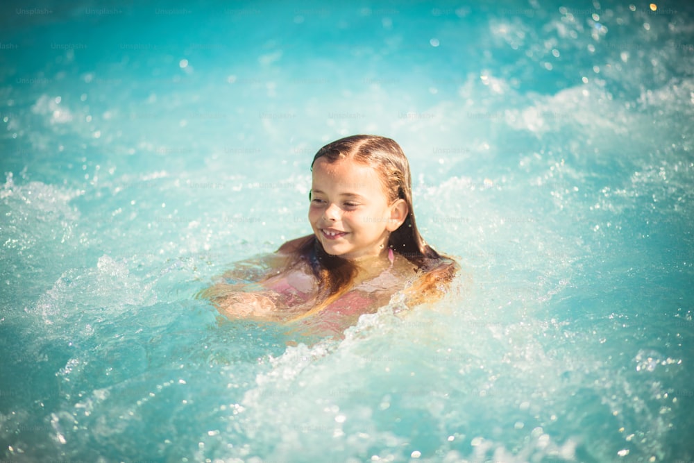 She enjoy in waves. Child swimming in the pool.
