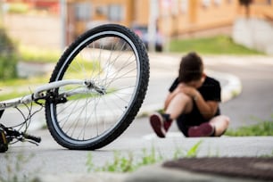 Kid se lastima la pierna después de caerse de su bicicleta. El niño está aprendiendo a andar en bicicleta. Niño en el suelo de la calle con una lesión en la rodilla gritando después de caerse de su bicicleta.