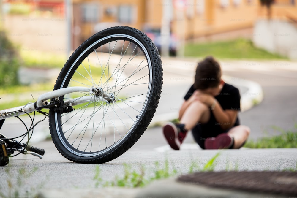 Kid hurts his leg after falling off his bicycle. Child is learning to ride a bike. Boy in the street ground with a knee injury screaming after falling off to his bicycle.