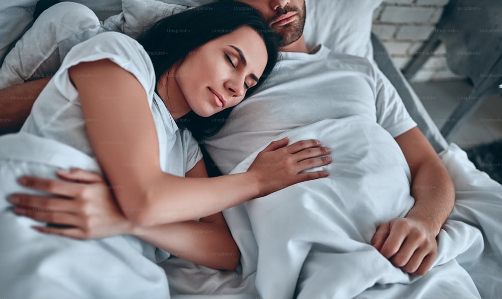 Good morning! Young couple in bedroom. Handsome bearded man and attractive young woman sleeping together in bed.