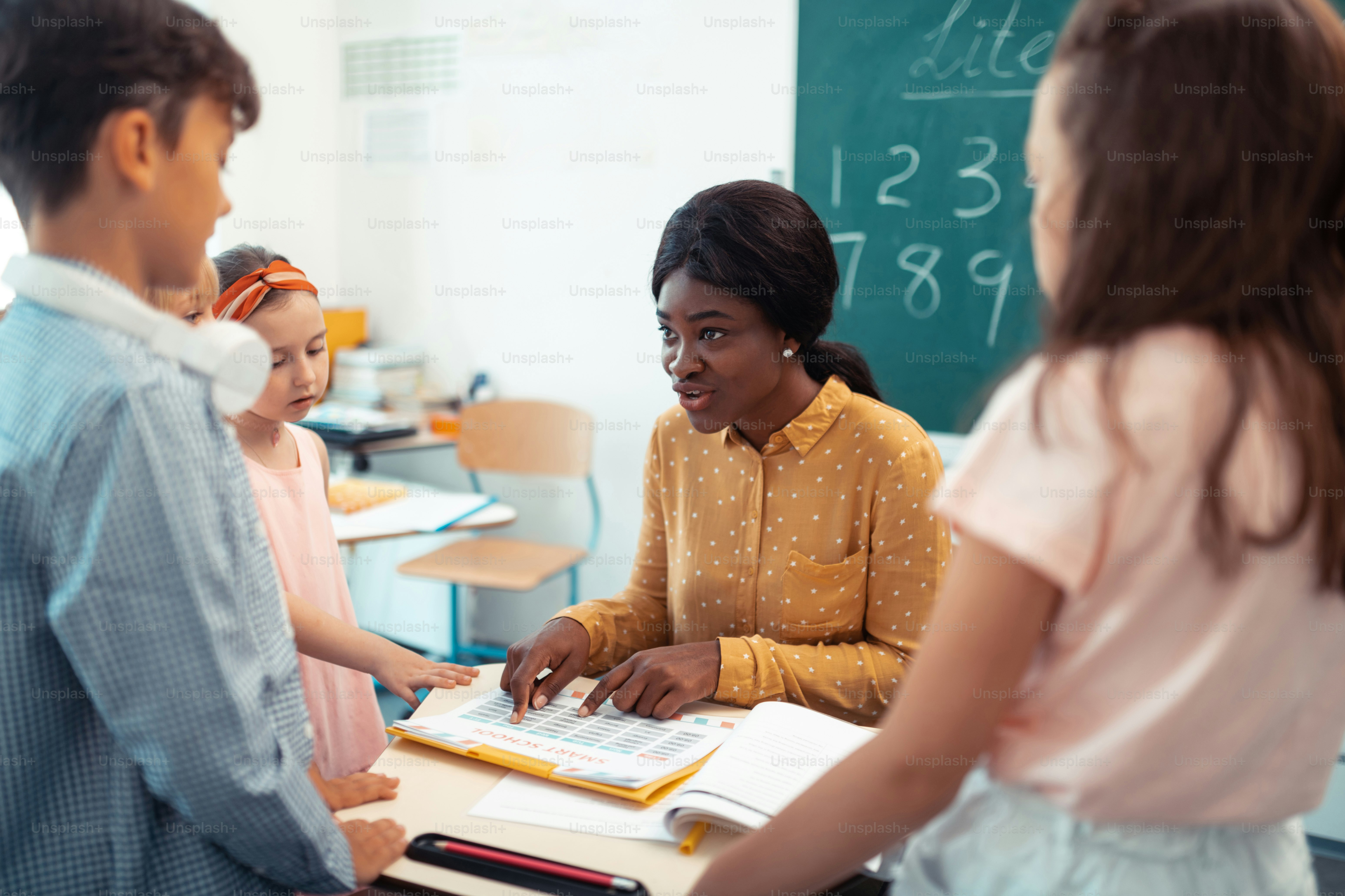 Escola primária. Profissional atraente professor de pele escura da escola primária falando com os alunos
