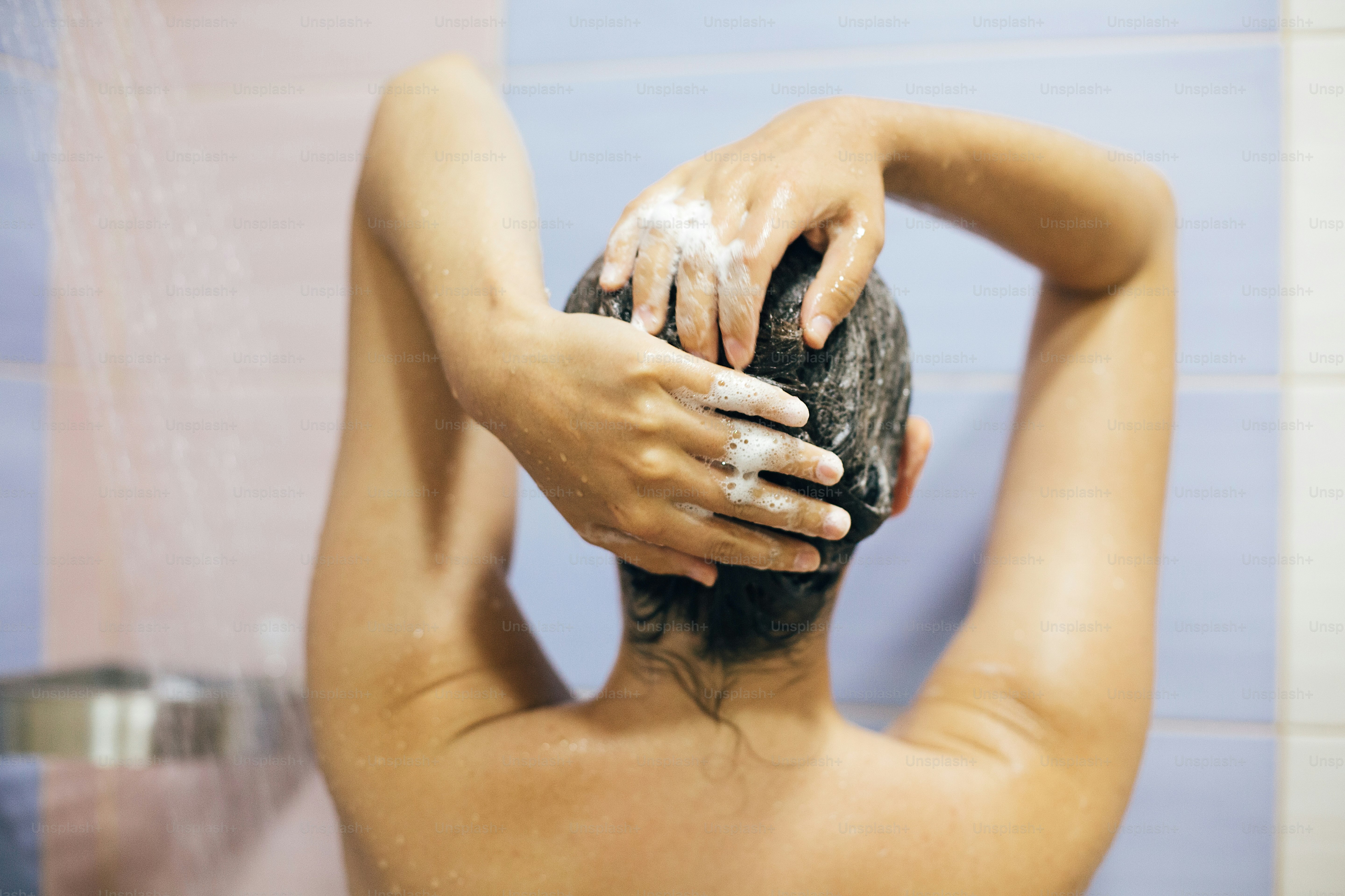 Young happy woman washing her hair with shampoo, hands with foam closeup. Back of beautiful brunette girl taking shower and enjoying relax time. Body and hair hygiene, lifestyle concept