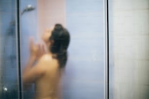 Blurred defocused image of  happy woman taking hot shower at home or hotel bathroom.Beautiful brunette girl enjoying time in shower. Body and skin hygiene, lifestyle concept. Space text