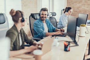 Waist up portrait of smiling man staying in call center while sitting at table and talking with female colleague