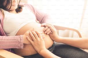 Pregnant couple of husband and wife feels love and relax at home. Young expecting woman holds baby in pregnant belly. Father take care of pregnant mother. Concept of maternity and pregnancy care.