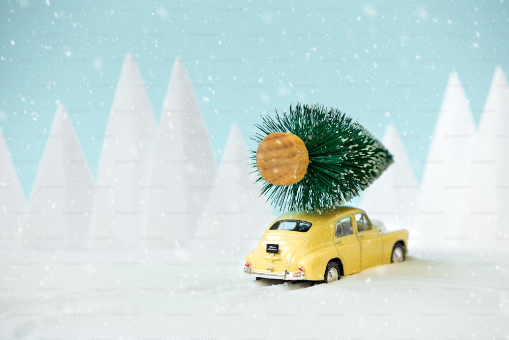 Retro car toy carrying Christmas fir tree in snowy landscape. Christmas or New Year celebration concept. Copy space. Selective focus