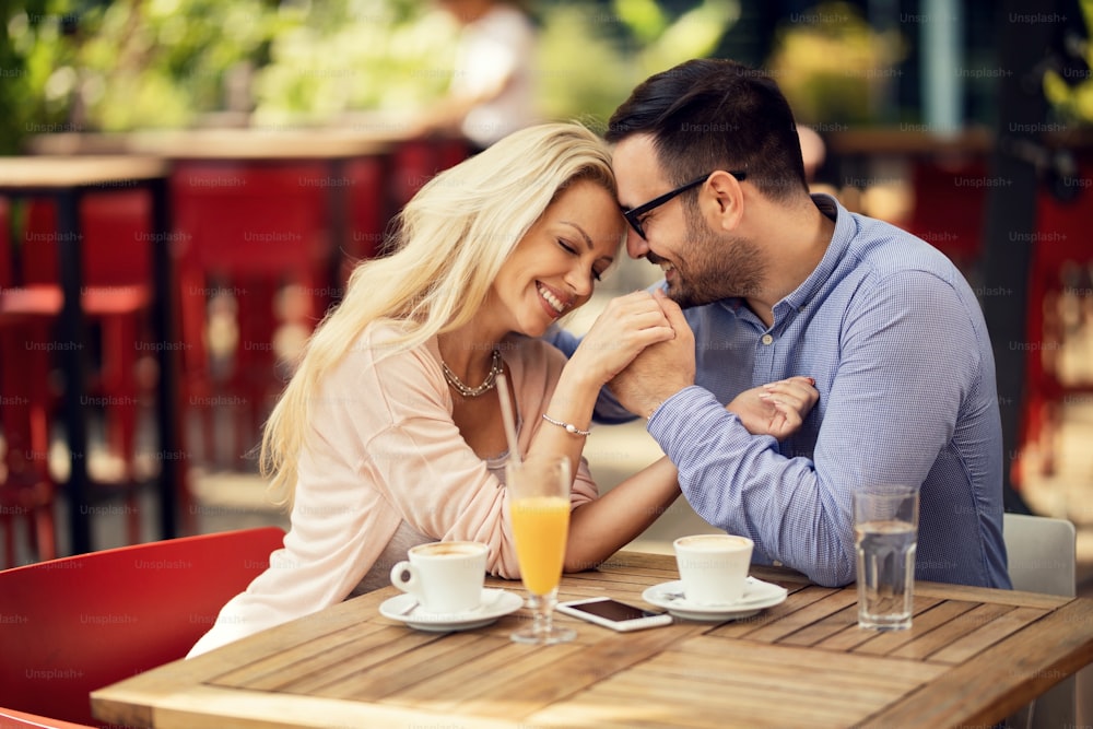 Smiling couple in love showing affection to each other while holding hands with their eyes closed in a cafe.