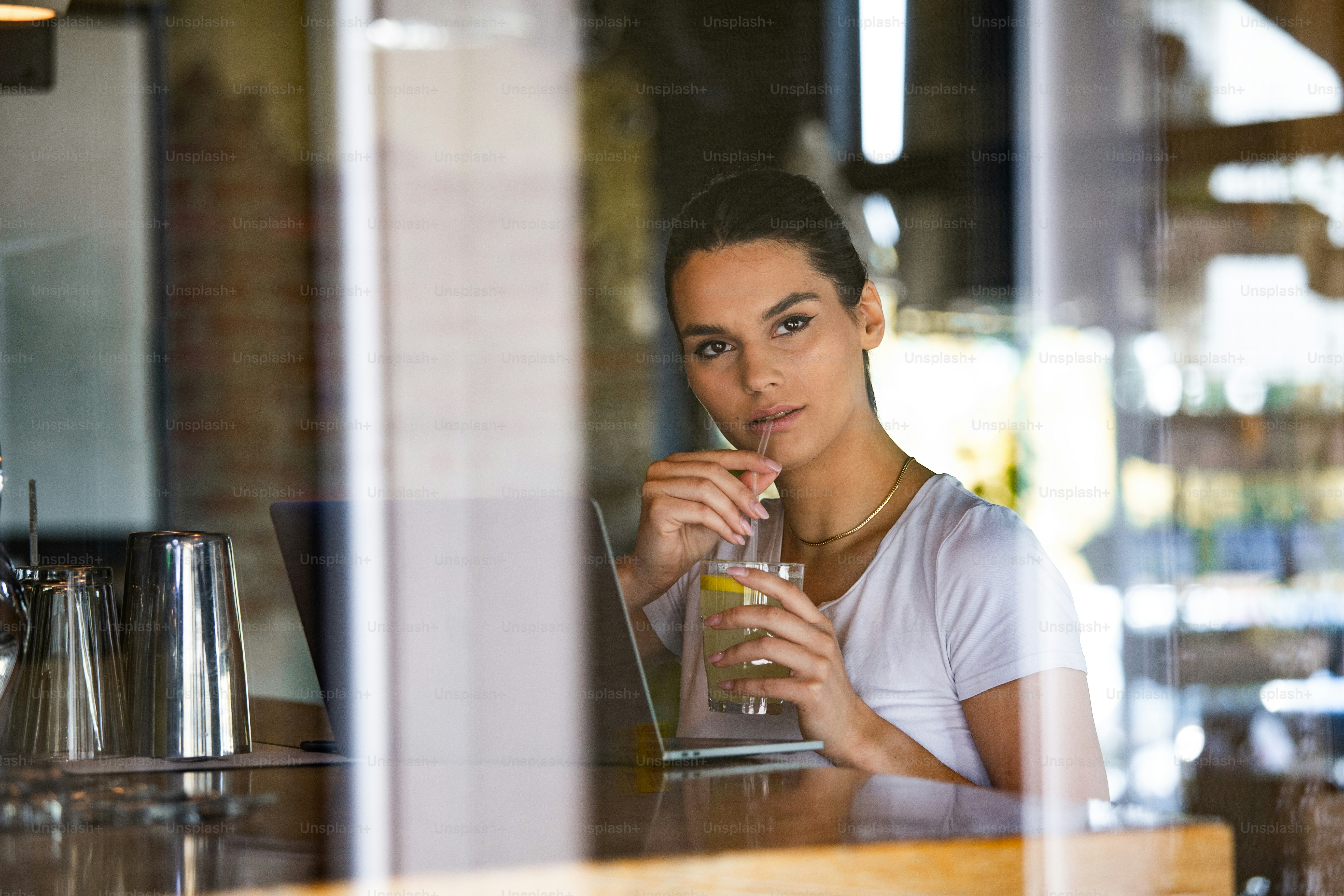 Beautiful woman is thinking about something good, while is waiting file downloads on her laptop computer. Pretty female student is enjoying juice, while is resting after video conference via net-book