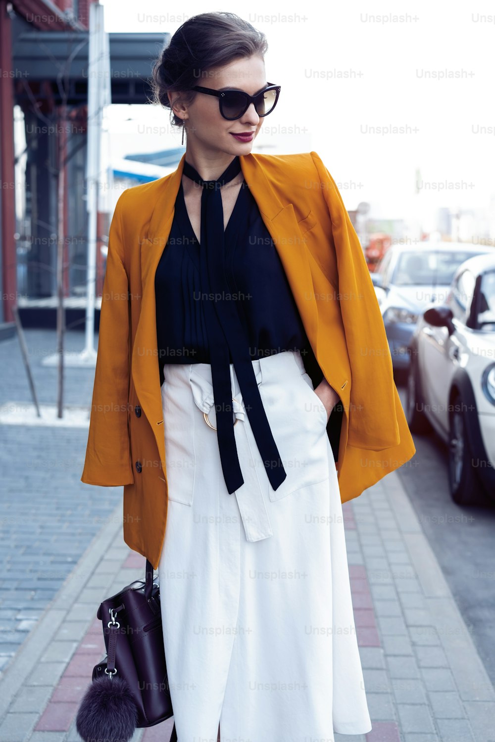 Portrait fashion woman in sunglasses walking on street . She wears yellow jacket, smiling to side