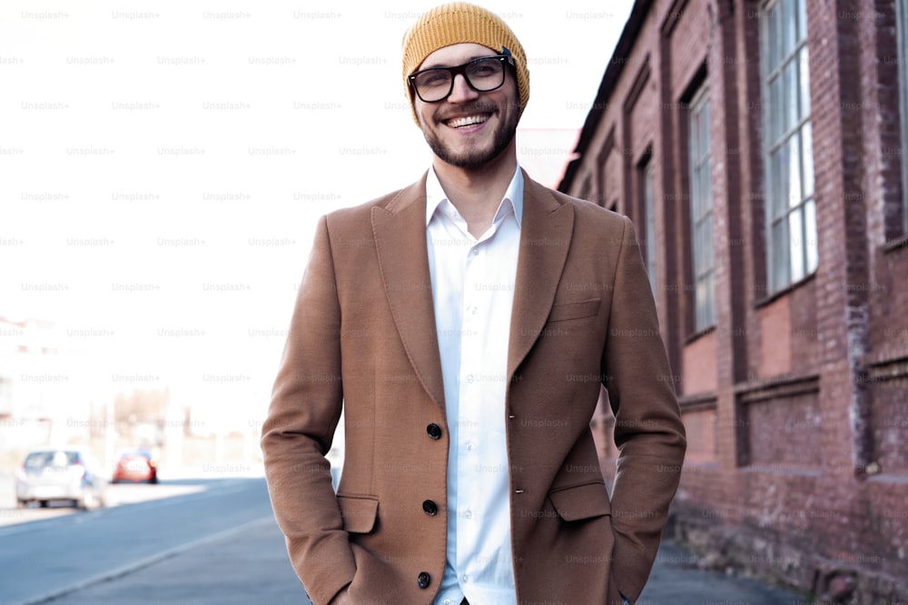 Portrait of stylish handsome young man in glasses with bristle standing outdoors. Man wearing jacket and shirt